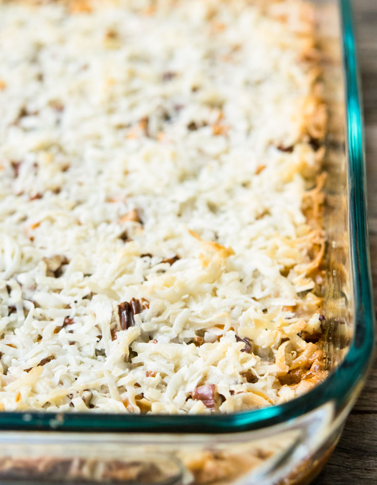 These one pan 7 Layer Bars are crunchy and gooey…just what you need to satisfy that sweet tooth. Whip them up for your next get together! #7layerbars #cookiebars 7 Layer Bars in a glass baking dish