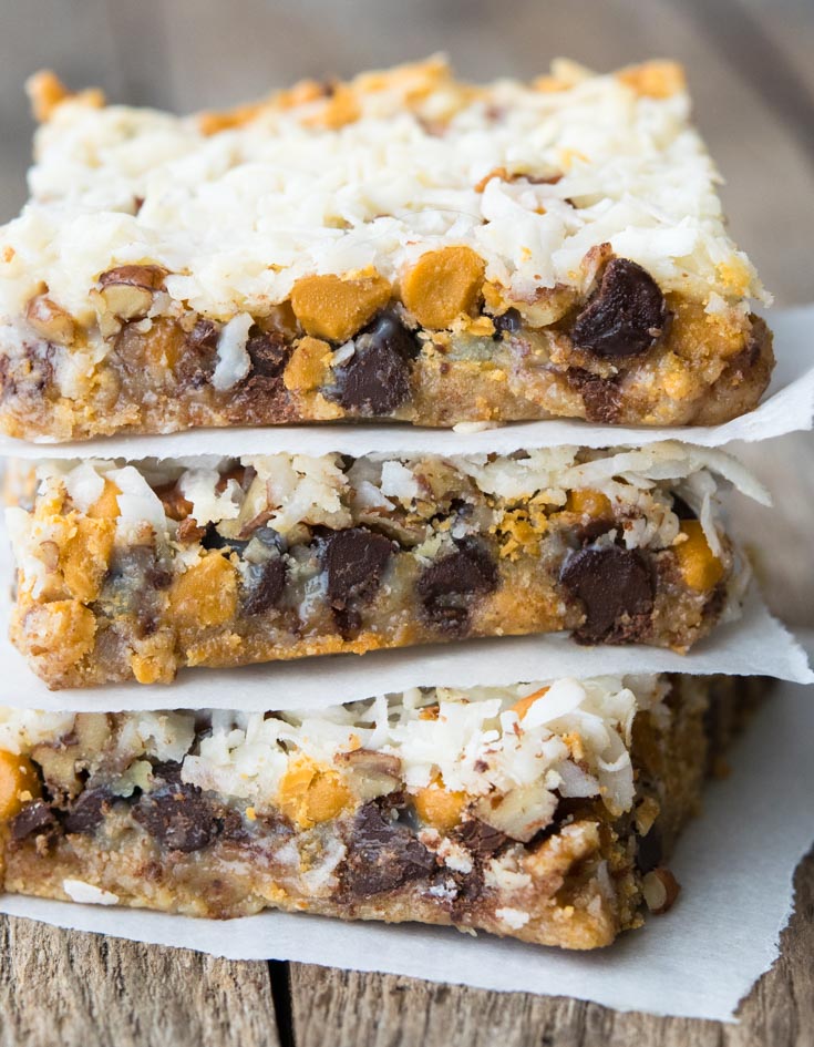 These one pan 7 Layer Bars are crunchy and gooey…just what you need to satisfy that sweet tooth. Whip them up for your next get together! #7layerbars #cookiebars 7 Layer Bars stacked on top of each other