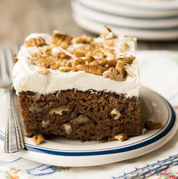 A single serving of Applesauce Cake with frosting and chopped pecans on top, on a saucer