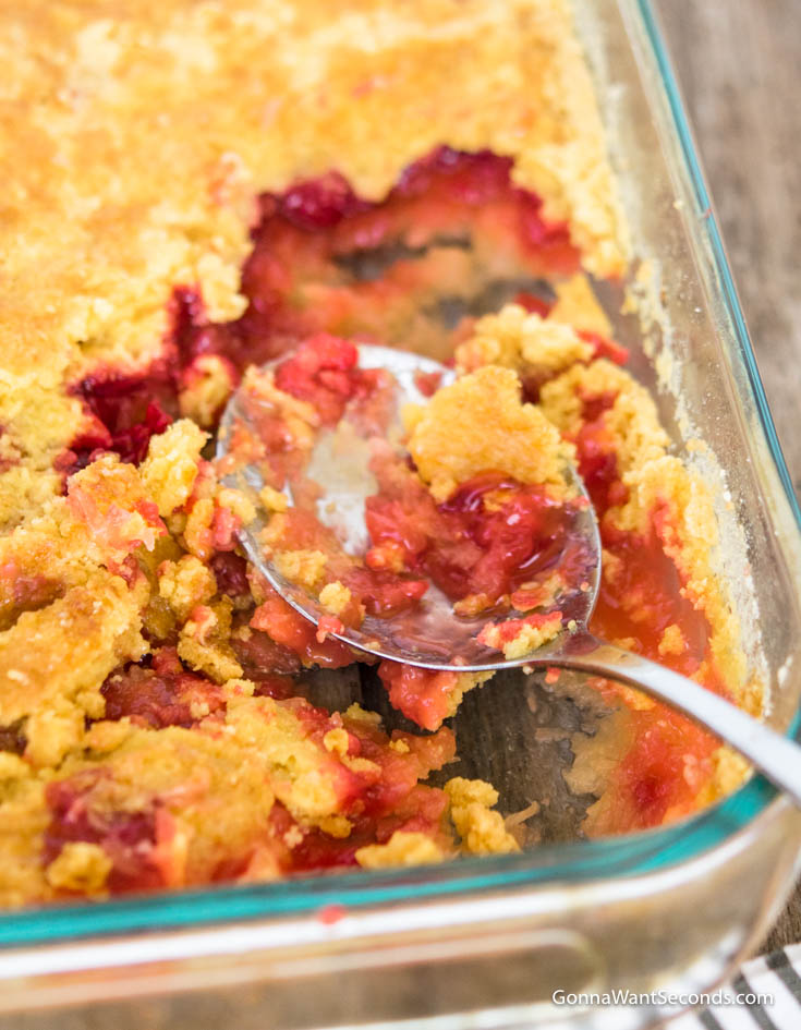 Scooping cherry pineapple dump cake in a casserole dish