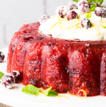 Cranberry Jello Salad with Lemon Cream Topping, garnished with sugared cranberries and mint leaves, on a cake stand