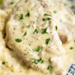 Crock Pot Ranch Pork Chops smothered in creamy gravy and topped with chopped parsley, on a plate