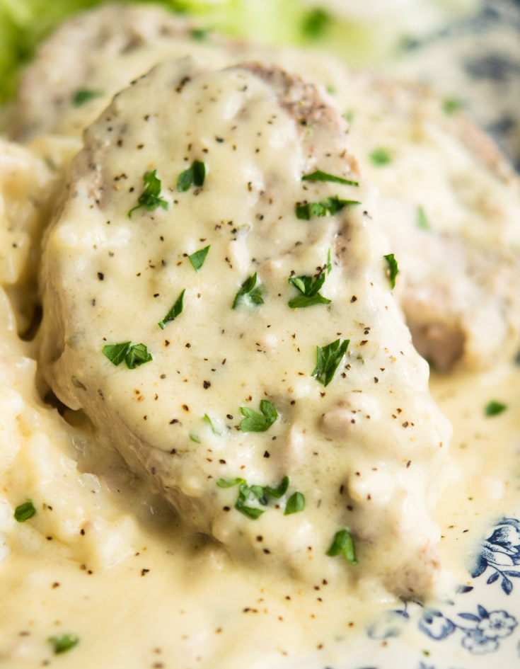 Crock Pot Ranch Pork Chops smothered in creamy gravy and topped with chopped parsley, on a plate
