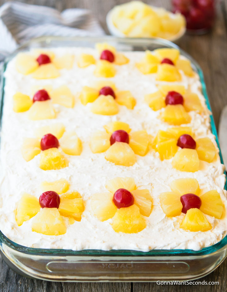 southern pineapple sunshine cake with whipped topping, topped with pineapples and cherries in 9x13 sheet pan