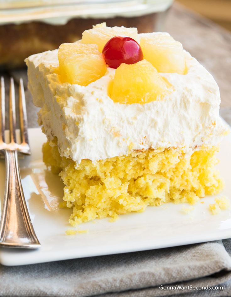 A slice of easy pineapple sunshine cake with whipped topping, topped with pineapple and cherry on a plate