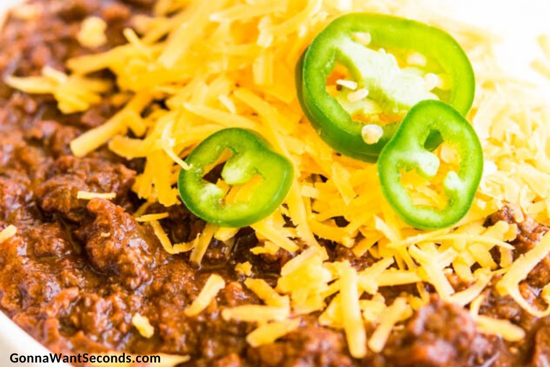 texas chili with ground beef recipe topped with shredded cheese, sour cream and jalapenos, in a bowl