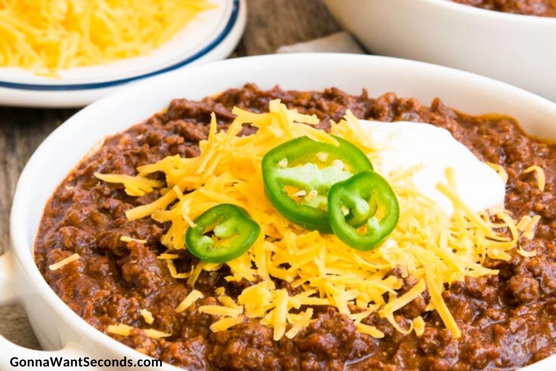 award winning texas chili recipe topped with shredded cheese, sour cream and jalapenos, in a bowl