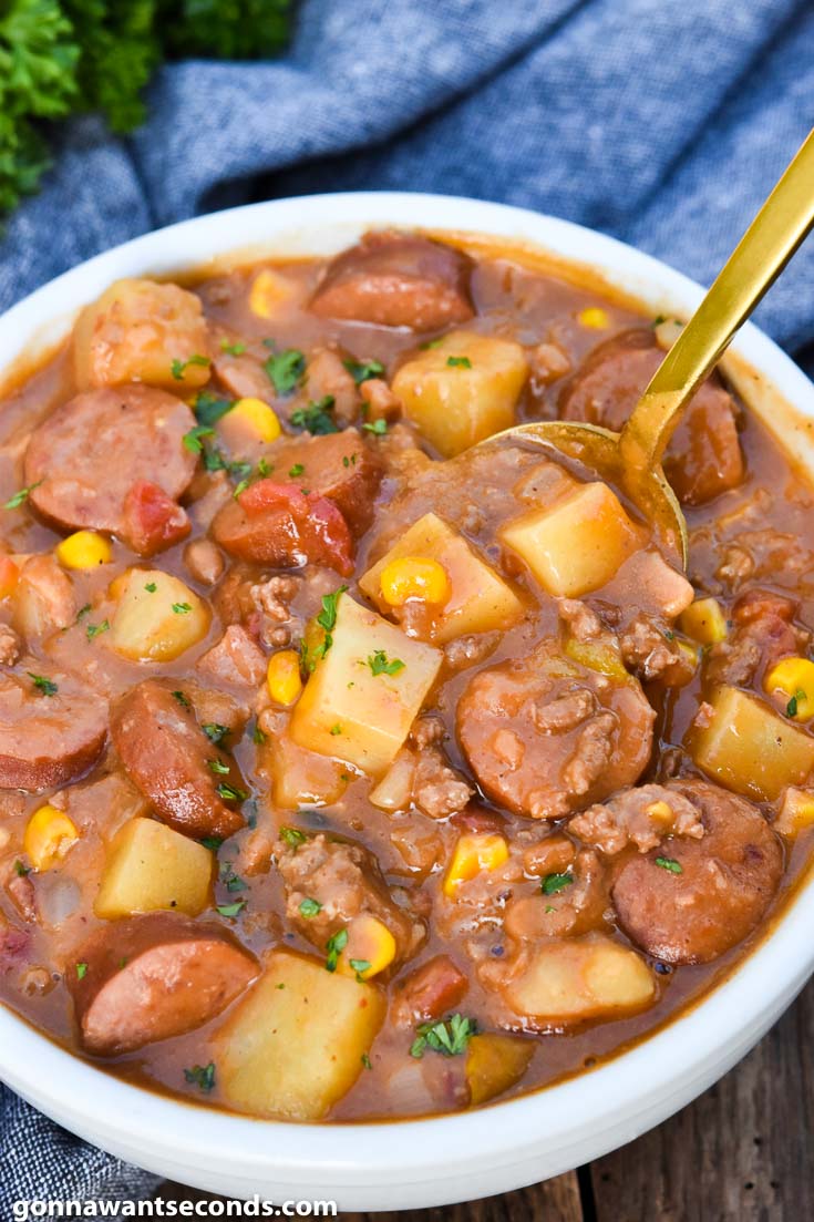 Spoon scooping cowboy stew with sausage in a bowl