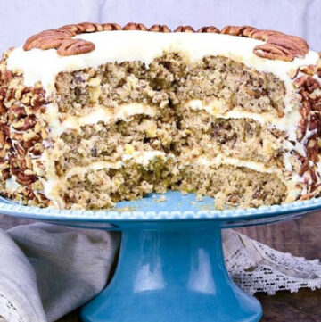 hummingbird cake with a few slices removed showing the layers inside, on a cake stand