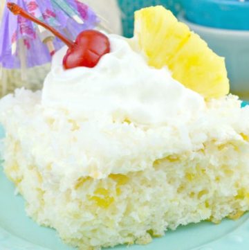 A slice of Pina Colada Cake with frosting, topped with a cherry, a pineapple, and a cocktail umbrella