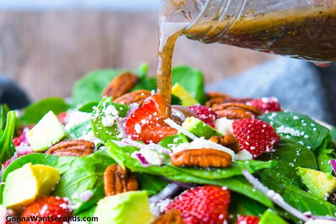 Pouring balsamic vinaigrette over strawberry spinach salad