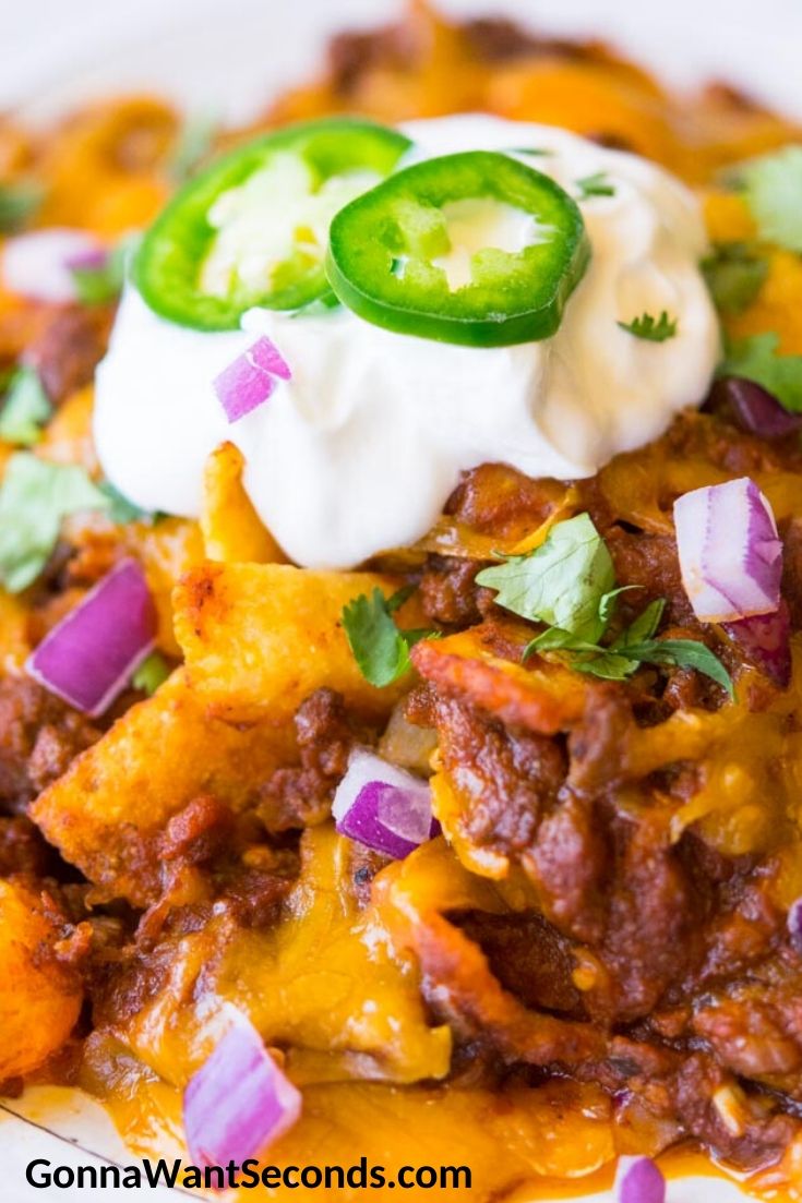 Frito pie topped with a dollop of sour cream and slices of jalapenos