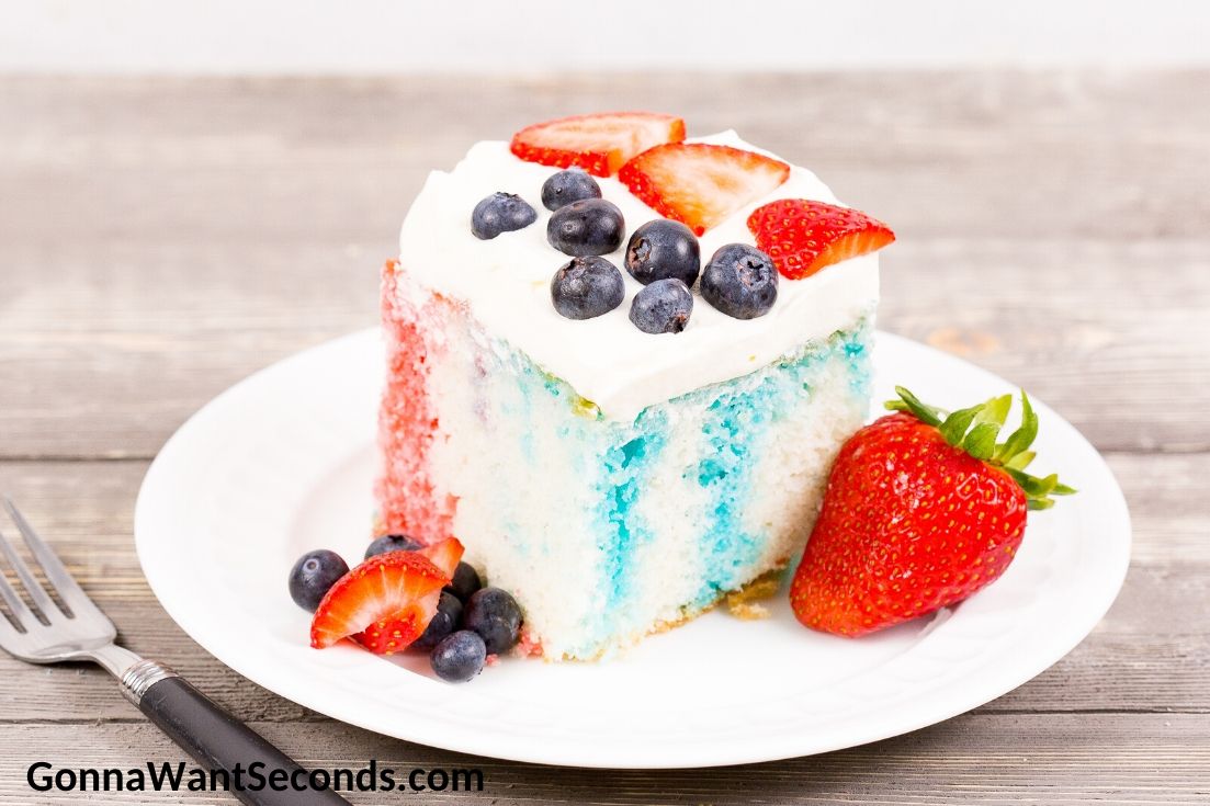 A slice of Red White and Blue Poke Cake topped with strawberries and blueberries, on a plate