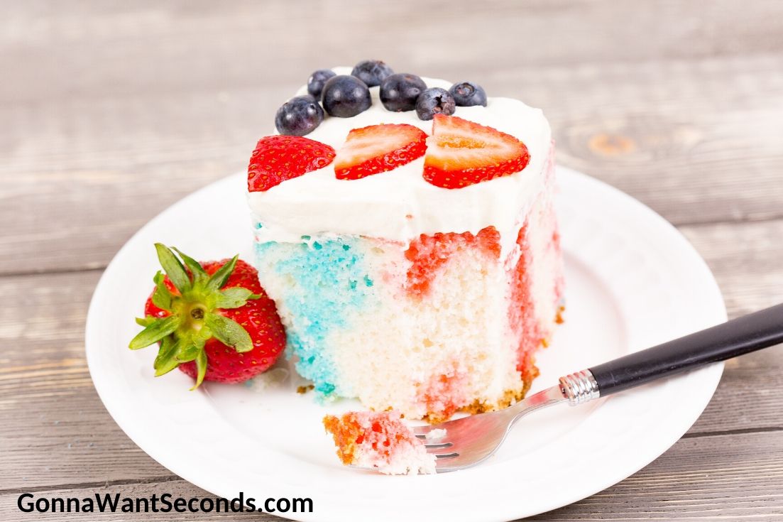 A slice of Red White and Blue Poke Cake topped with strawberries and blueberries, on a plate