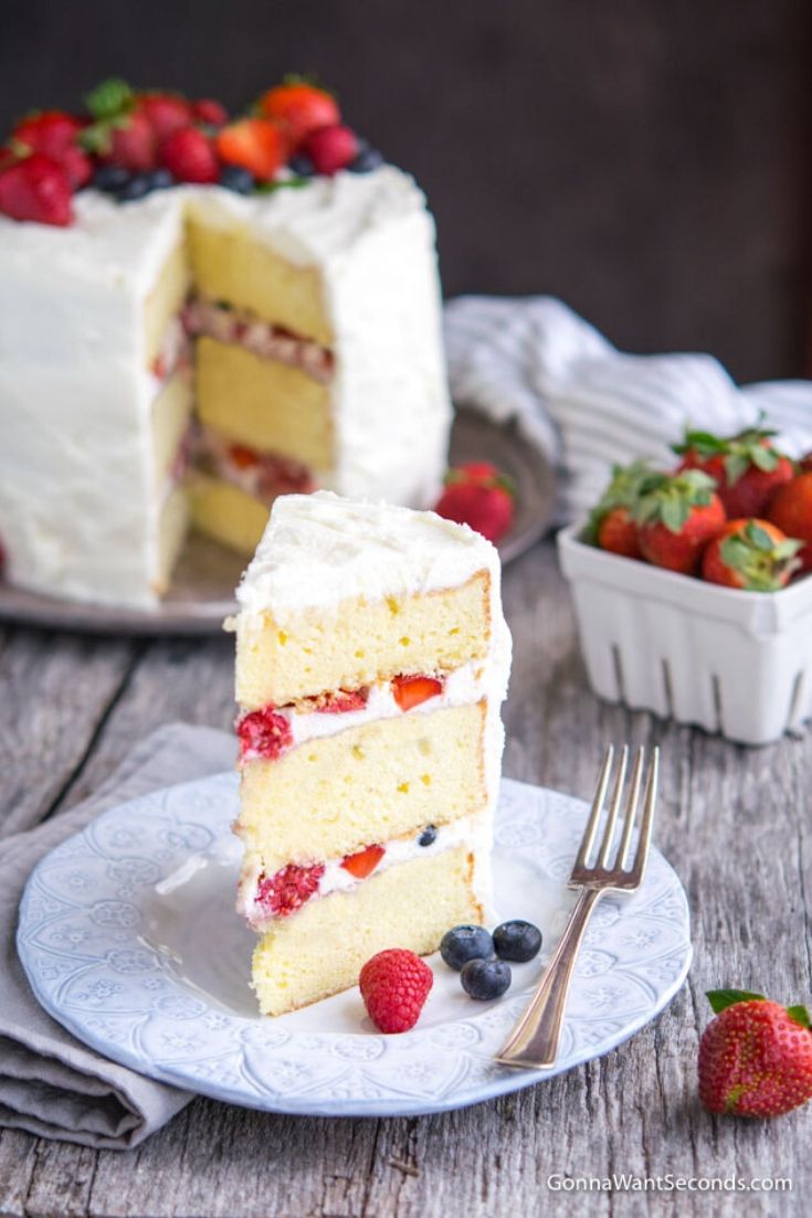 A slice of Berry Chantilly Cake with the whole cake at the back