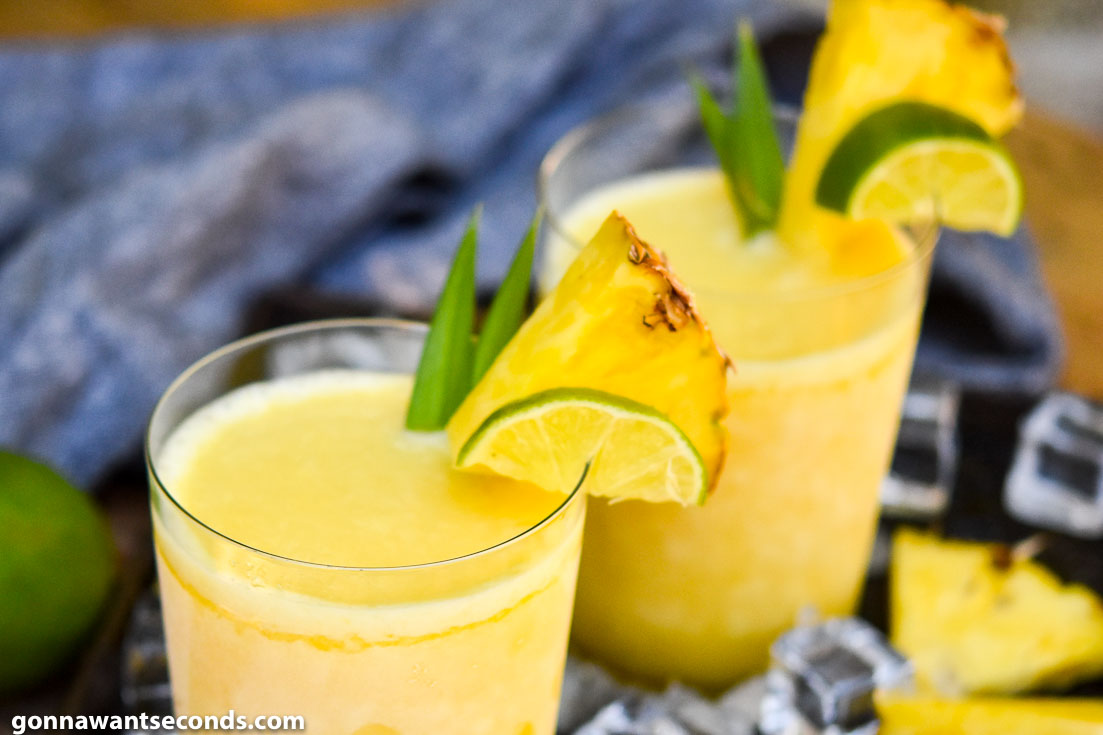 Two glasses of Pineapple Margaritas topped with a slice of pineapple and lime