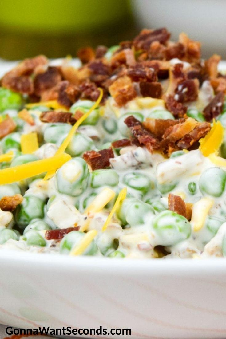 Pea Salad topped with bacon bits and shredded cheese, in a shallow bowl