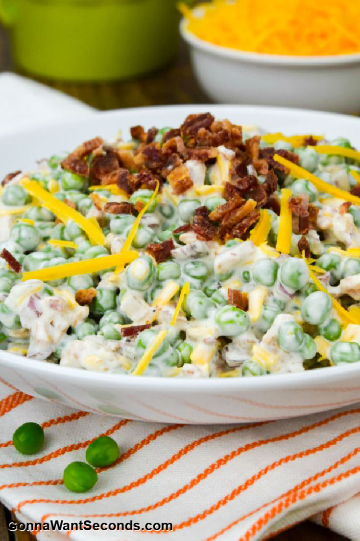 Green Pea Salad topped with bacon bits and shredded cheese, in a shallow bowl