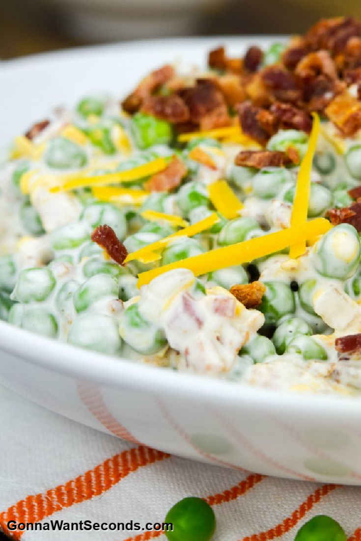 Creamy Pea Salad topped with bacon bits and shredded cheese, in a shallow bowl