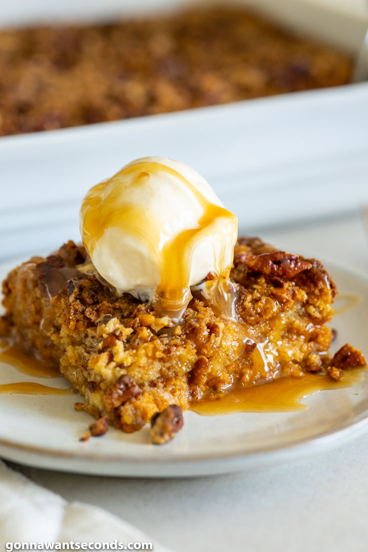 A slice of pumpkin dump cake with pecans, topped with vanilla ice cream and drizzled with caramel