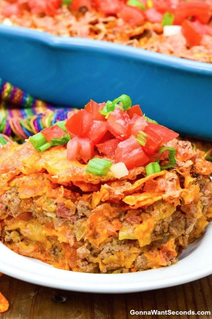 A slice of Dorito casserole topped with tomatoes on a plate