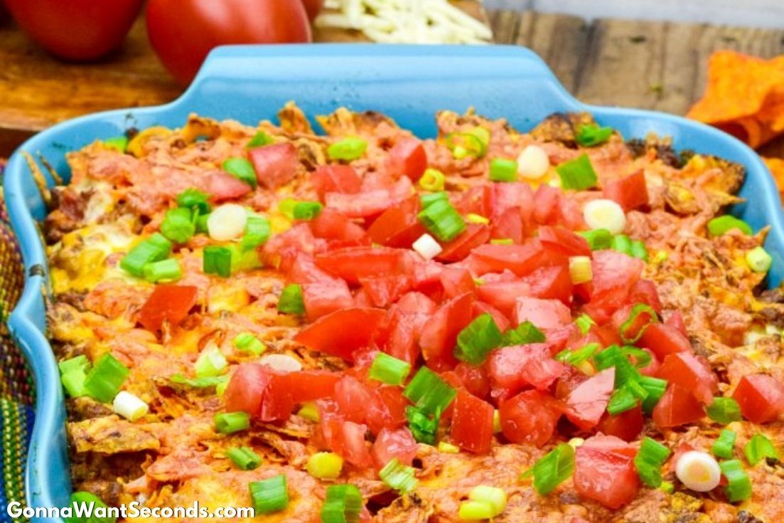 Dorito casserole topped with tomatoes on a blue casserole dish