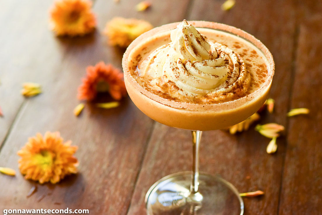 Pumpkin pie martini with whip cream on top with flowers on the table