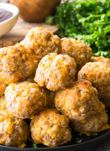 A pile of Bisquick Sausage Balls on a plate with dipping sauces on the side