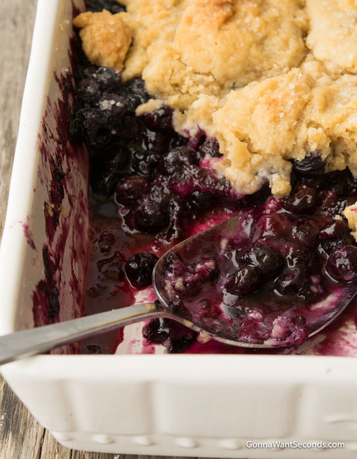 Spoon scooped some blueberry cobbler with frozen blueberries in a baking dish