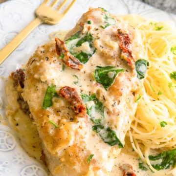 Creamy Tuscan Garlic Chicken on top of pasta, on a plate with fork on the side