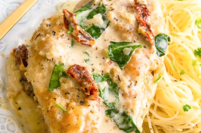 Creamy Tuscan Garlic Chicken on top of pasta, on a plate with fork on the side