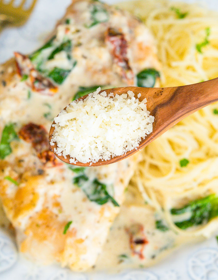 A spoonful of parmesan cheese close up, plate of Creamy Tuscan Garlic Chicken on the background