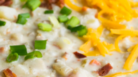 Crockpot Potato Soup topped with shredded cheddar cheese and bacon bits, in a black bowl