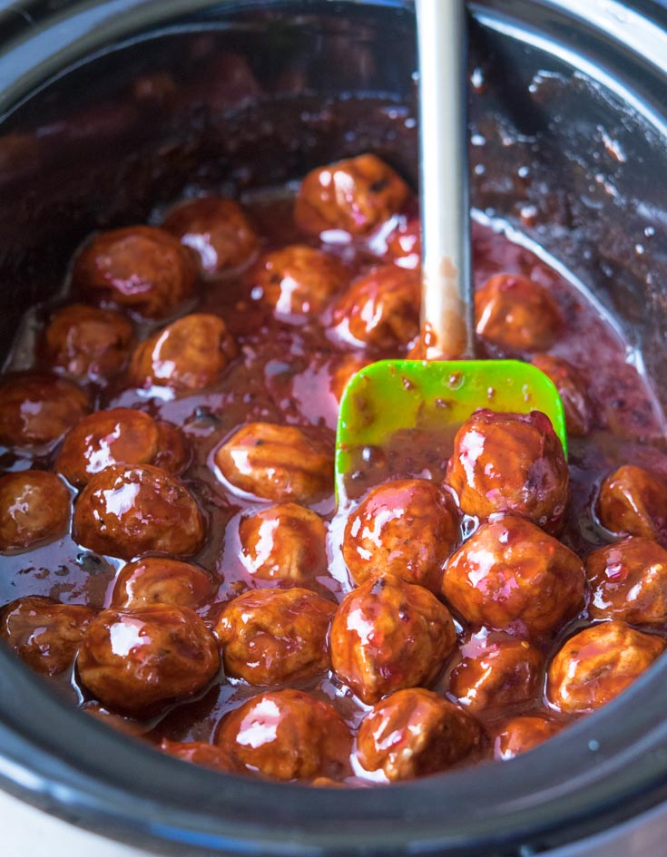 Rubber spatula mixing Grape Jelly Meatballs and sauce in a crockpot