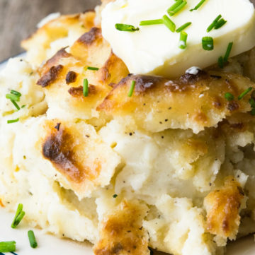 Make Ahead Mashed Potatoes topped with a slice of butter and chopped chive on a plate