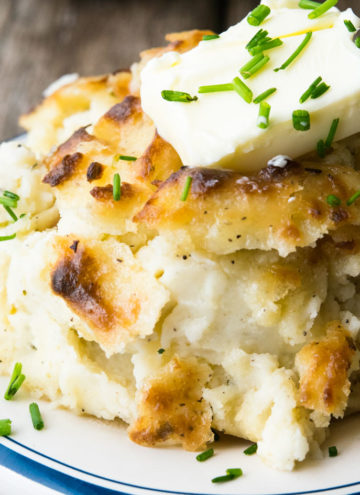 Make Ahead Mashed Potatoes topped with a slice of butter and chopped chive on a plate