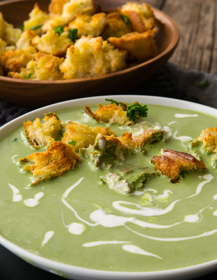 Spinach Soup with croutons and drizzle of heavy cream on top, in a white bowl