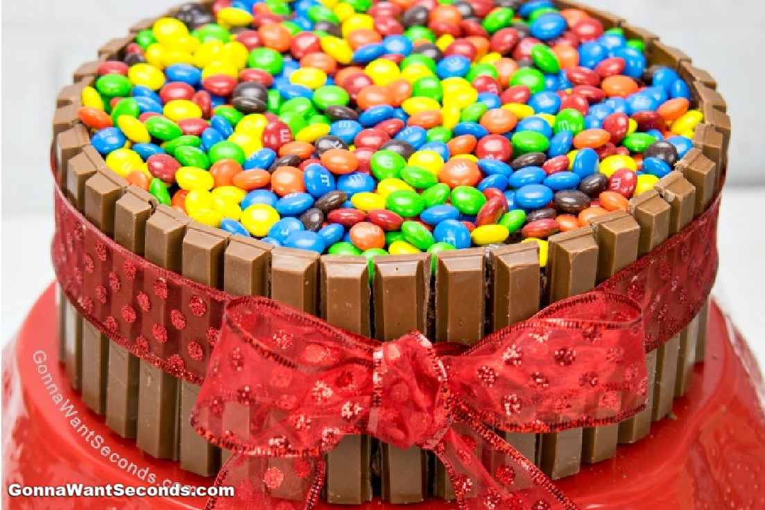 Kit Kat Cake tied around with a red ribbon with M&Ms on top, on a red cake stand