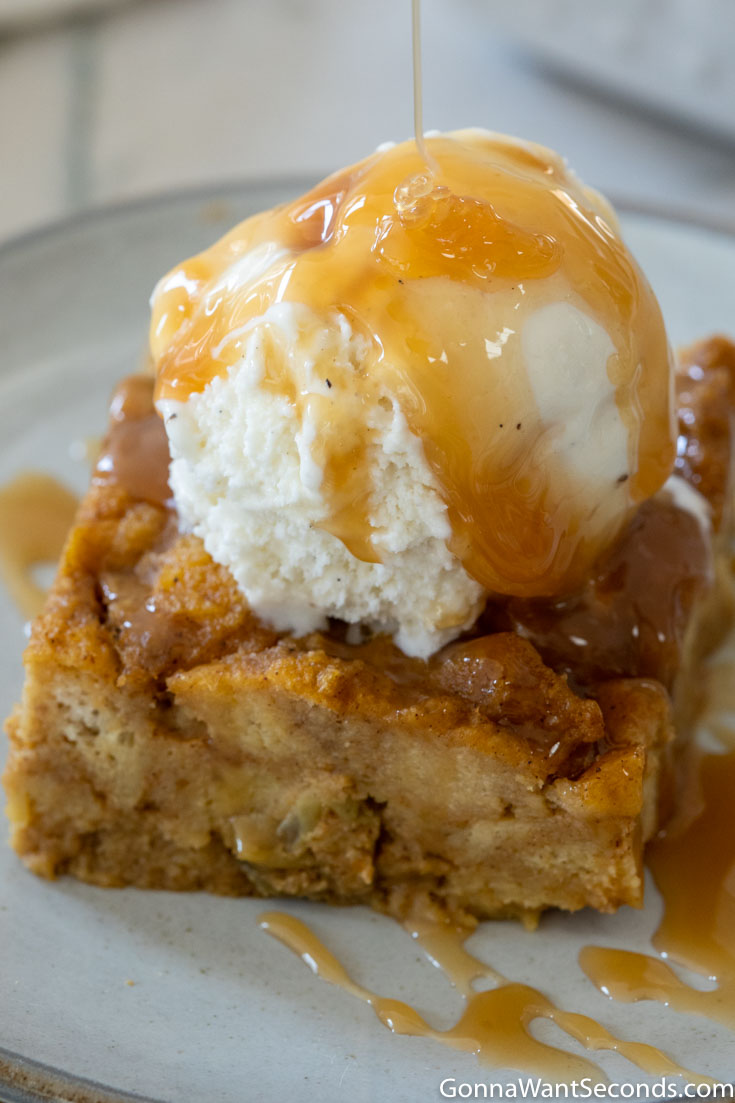 A slice of pumpkin bread pudding with a scoop of vanilla ice cream and caramel sauce