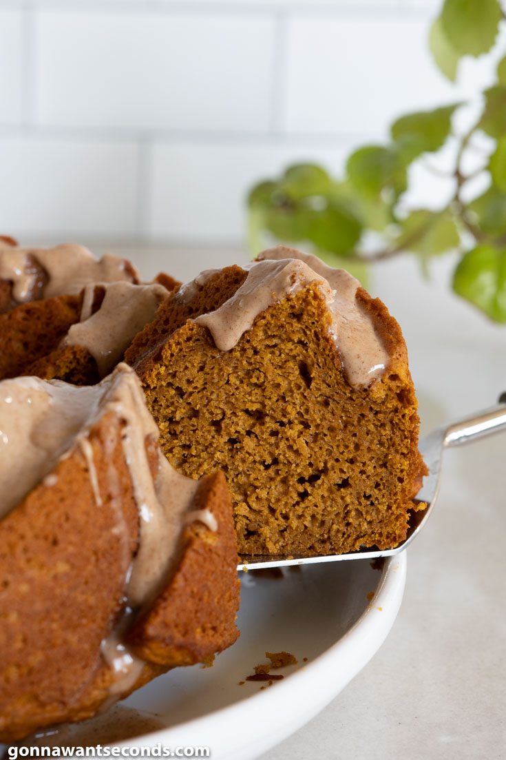 Lifting a slice of Pumpkin Bundt Cake with cinnamon glaze from the whole cake