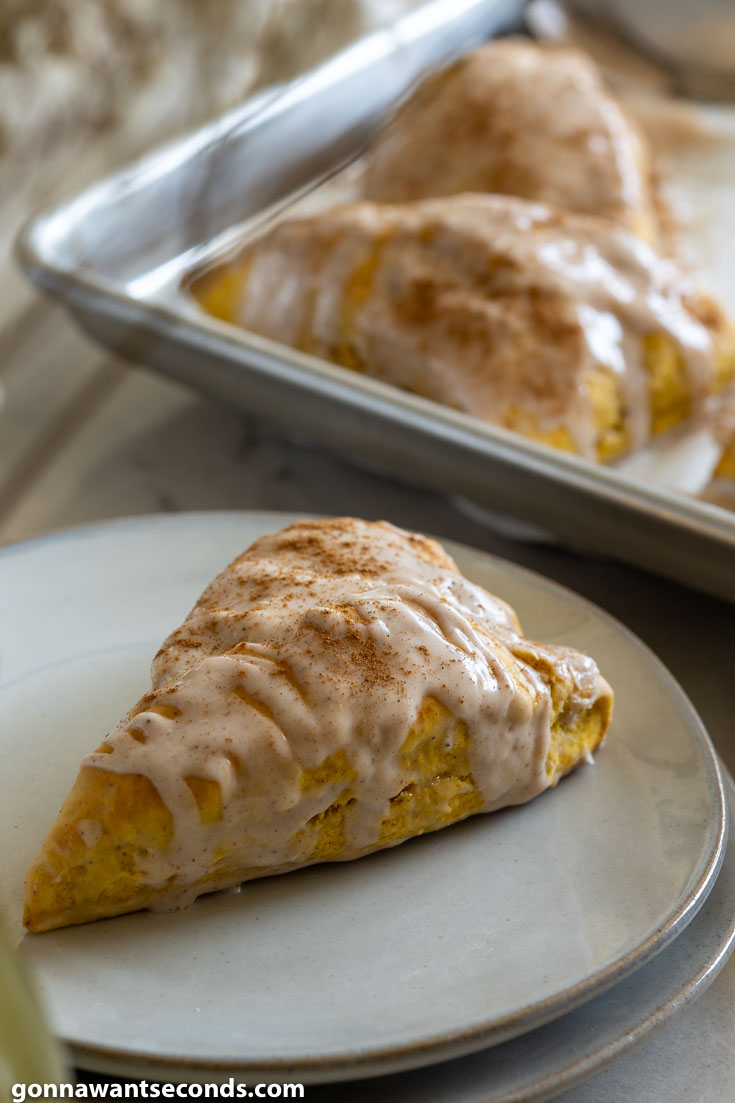 A slice of pumpkin recipes scones on a plate with a baking sheet full of scones at the back