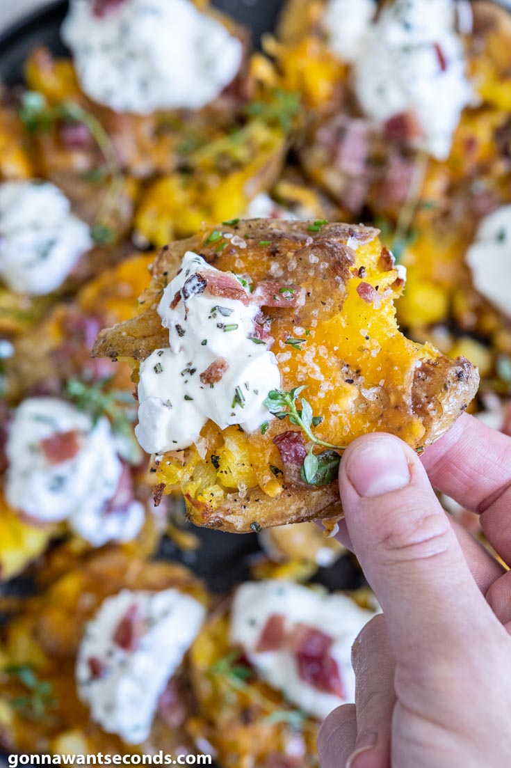 holding a piece of loaded crispy smashed potatoes with chive sour cream