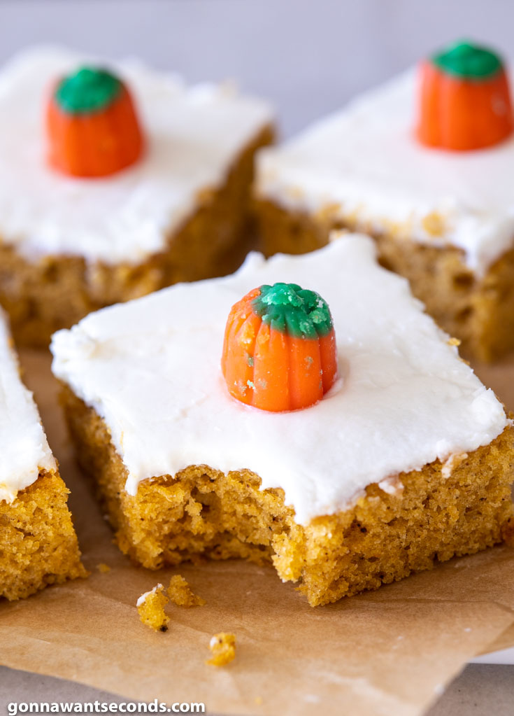 A slice of Pumpkin Bars with Cream Cheese Frosting with bite on the corner, decorated with candy pumpkin