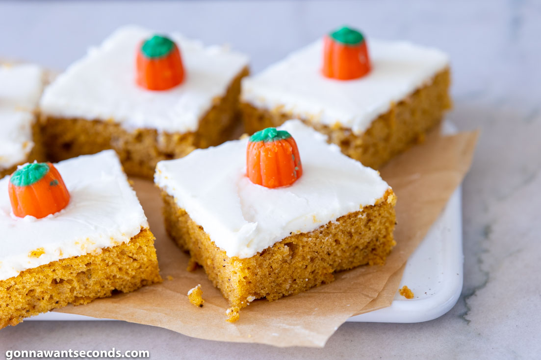 slices of healthy Pumpkin Bars with Cream Cheese Frosting, decorated with candy pumpkin on parchment paper