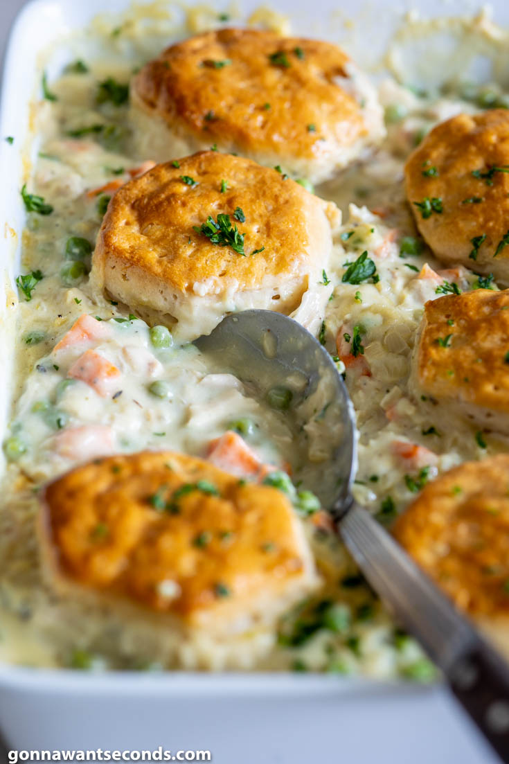 Scooping chicken pot pie with biscuits from the casserole