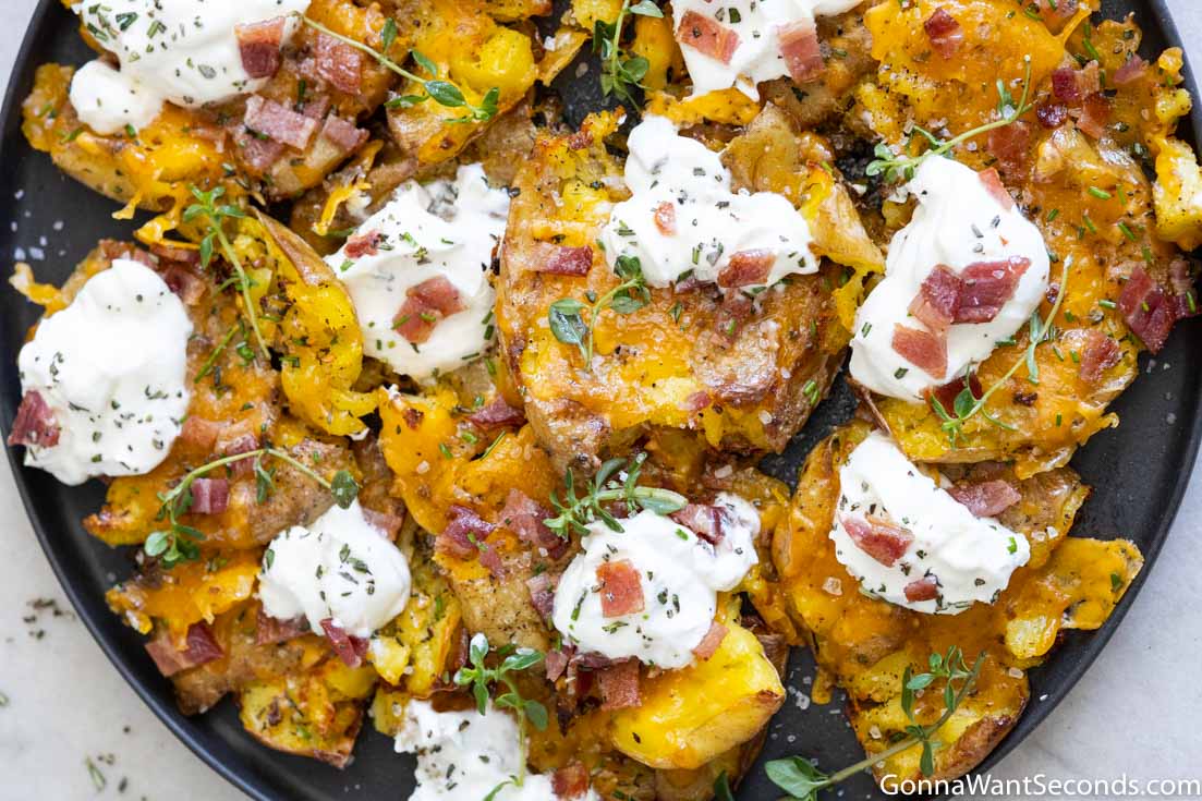 crispy smashed potatoes topped with sour cream and bacon on a plate, top shot
