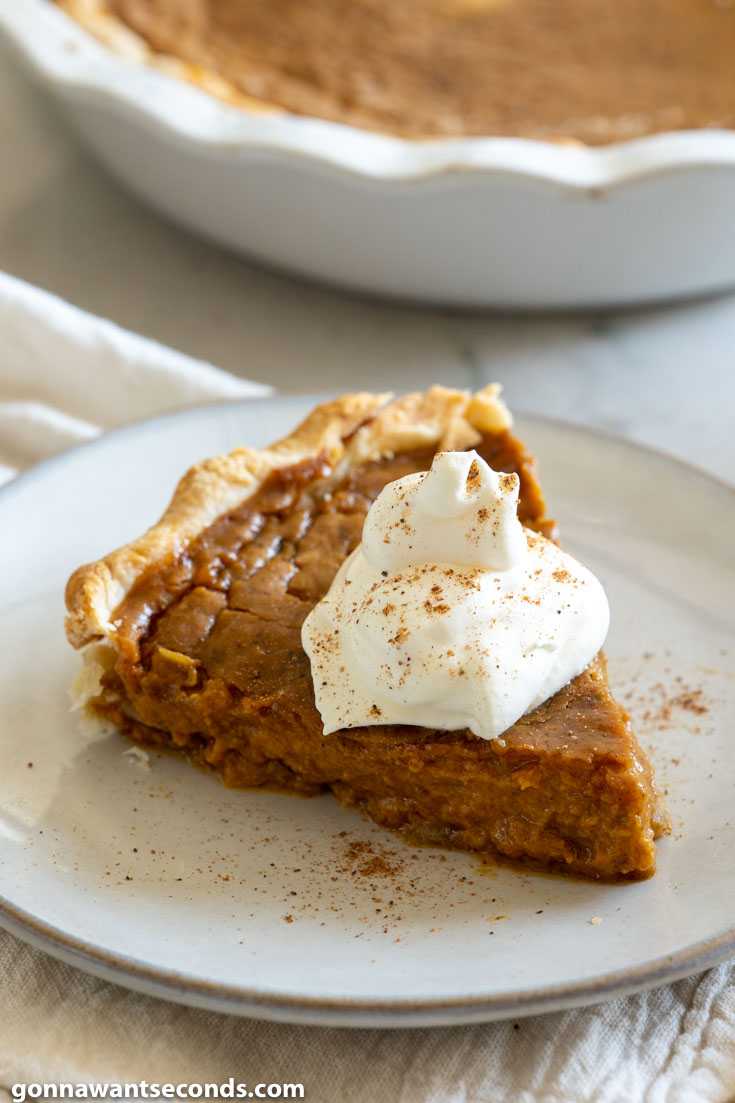 A slice of pumpkin pie topped with a dollop of whipped cream