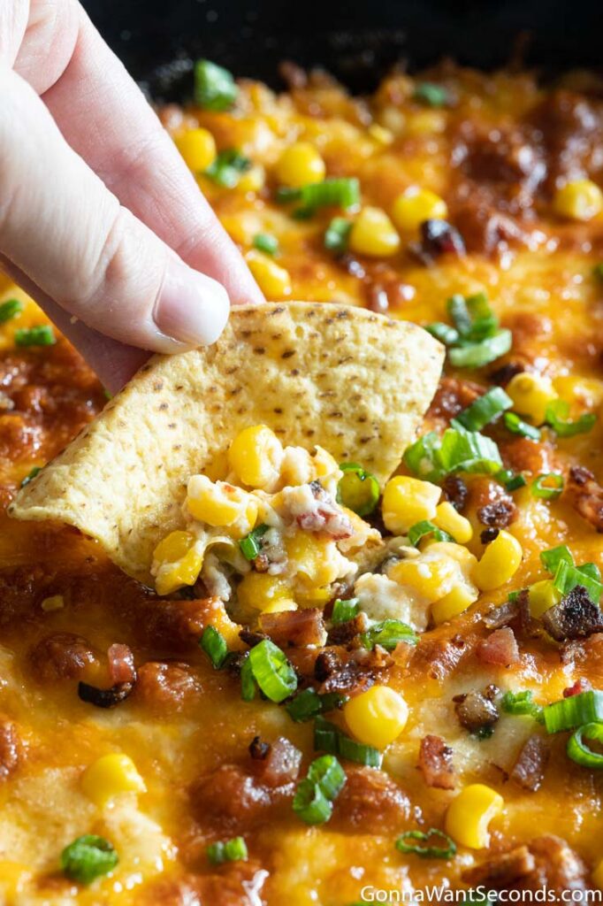 Hand holding a tortilla chip with cheesy hot corn dip recipe