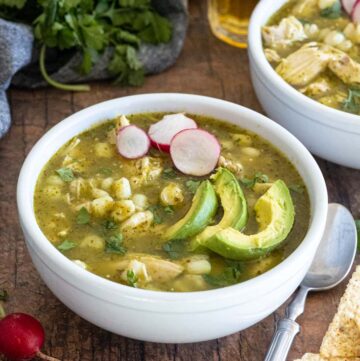 Bowls of pozole verde, topped with sliced avocados and radishes