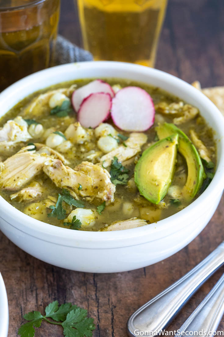 A bowl of pozole verde de pollo, topped with sliced avocados and radishes